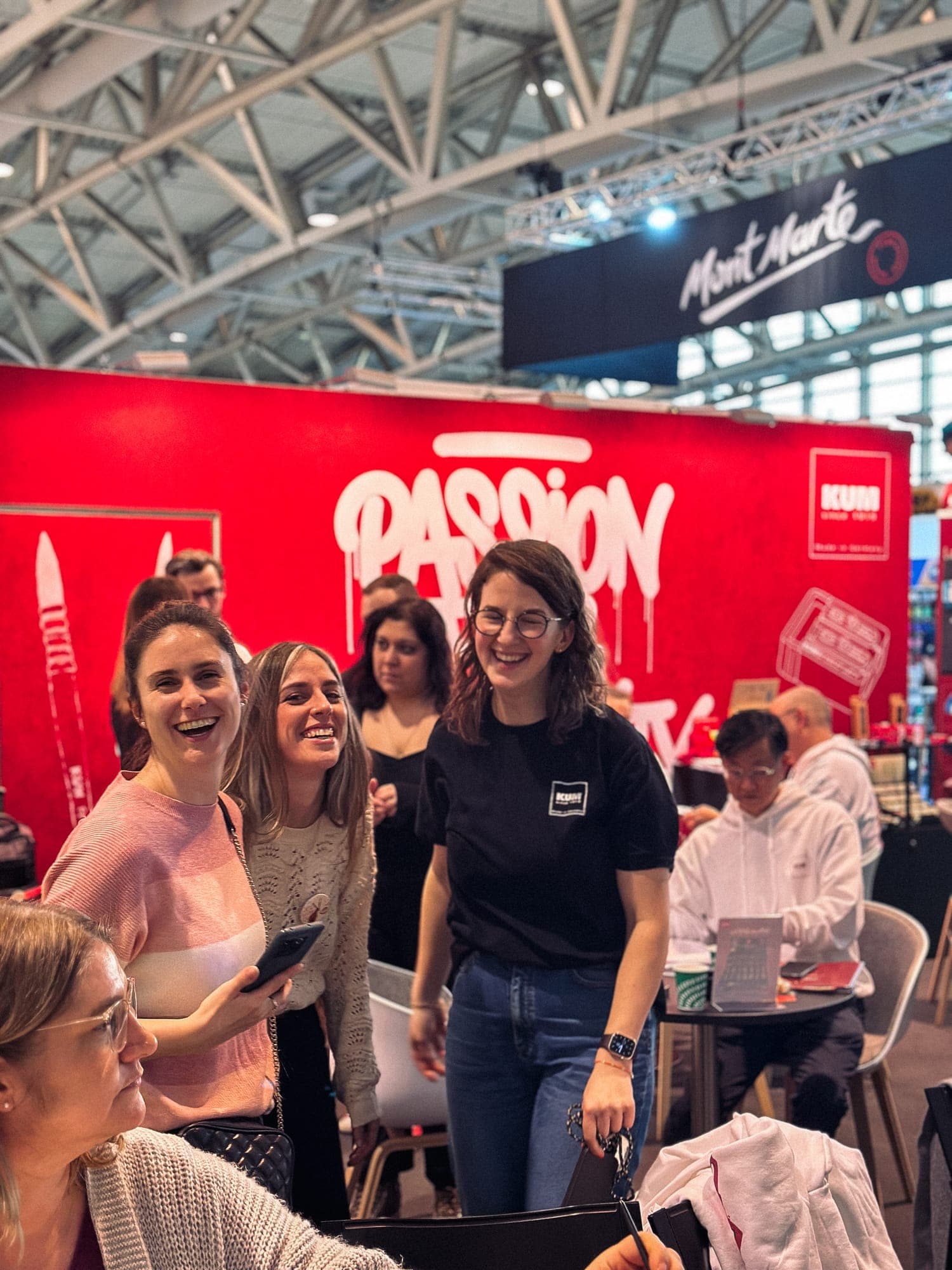 Besucherinnen und Team am roten KUM-Stand mit dem Schriftzug Passion for Creativity